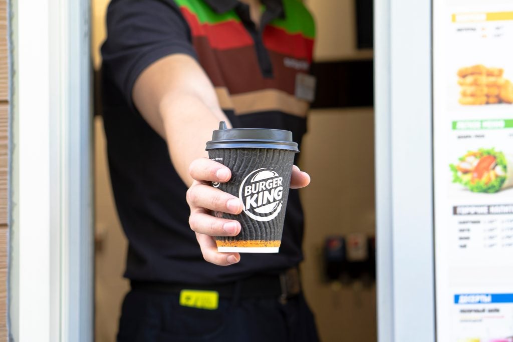 Burger King worker holding cup with a coffee. Hand with a paper cup coffee to go,  through the window of burger king car go,  take away service.