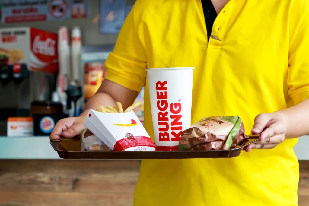 Man holding tray of Burger king set has whopper hamburger french fries and paper glass of cola drink in burger king restaurant self service.